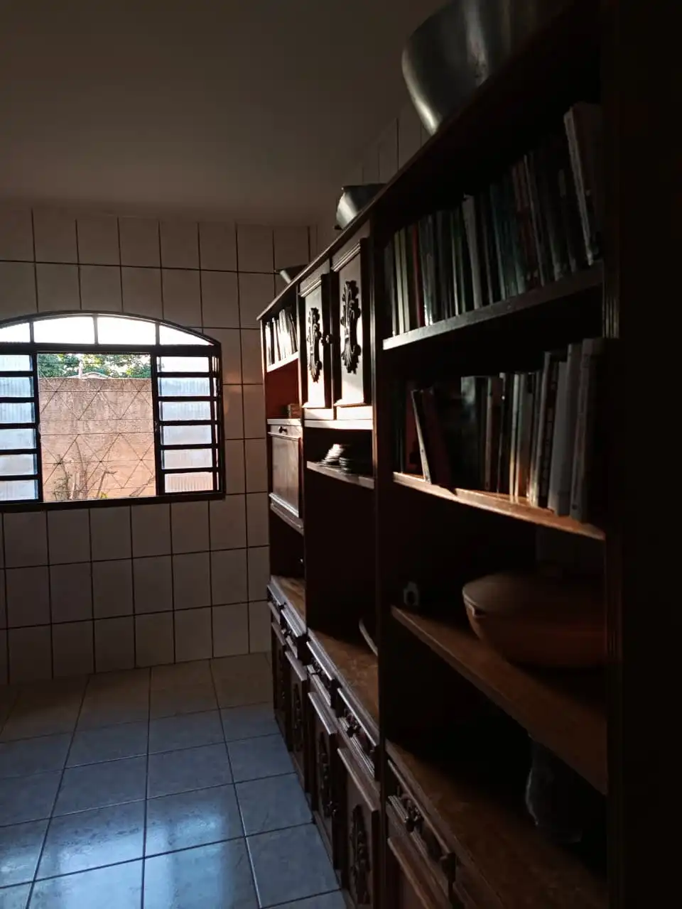 Estante de madeira com livros cristãos em uma sala iluminada pela luz natural da janela