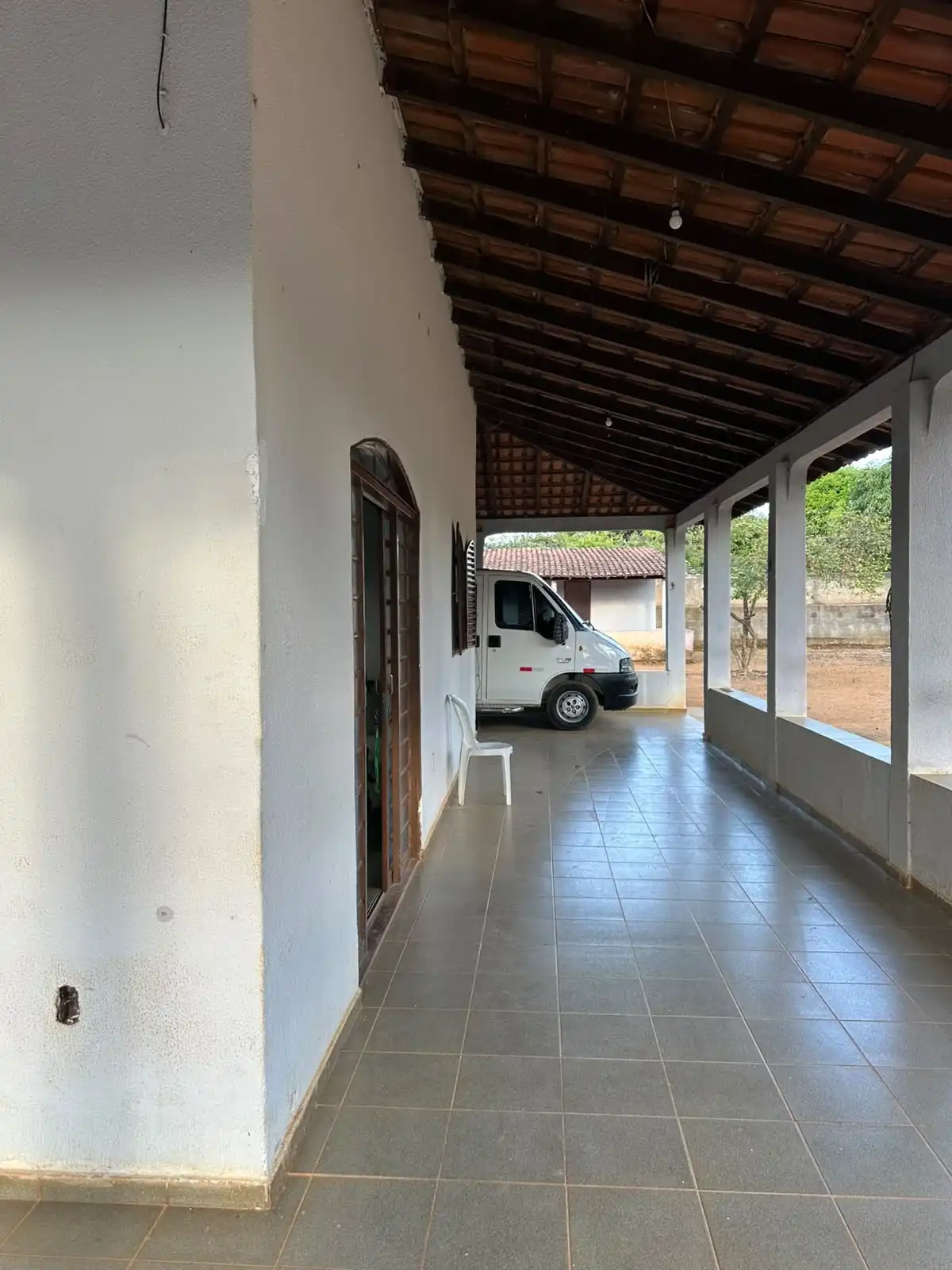 Varanda lateral da casa principal com piso cerâmico, porta em arco e vista para o terreno